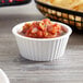 A white fluted Carlisle ramekin filled with salsa on a wood surface.