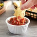 A person dipping a chip into a white fluted ramekin of salsa.