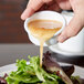 A person pouring sauce over a salad from a white Carlisle plastic ramekin.