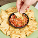 A hand dipping a chip into a Carlisle black salsa bowl.