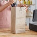 A woman opening a bottle of wine in a brown paper bag on a table.