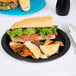 A sandwich and potato chips on a black Creative Converting paper plate.