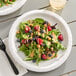 A white Creative Converting paper plate with salad, berries, and nuts on it.