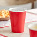 A close-up of a red Creative Converting paper cup with ice in it.