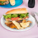 A sandwich with lettuce and tomato on a white paper plate with potato chips and corn.