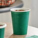 A close up of a Creative Converting Hunter Green paper cup with water droplets on it.
