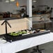 A black Carlisle double sneeze guard on a buffet table with food.