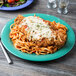 A GET Diamond Mardi Gras melamine plate with a plate of spaghetti and chicken with sauce on a wood table.