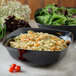 A Carlisle black melamine bowl filled with pasta and salad on a table in a salad bar.