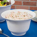 A Tablecraft white cast aluminum tulip salad bowl filled with salad on a table.