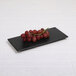 A black rectangular Elite Global Solutions melamine tray with a bunch of red grapes on it.