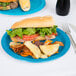 A sandwich with lettuce and tomato and potato chips on a turquoise blue Creative Converting paper plate.