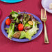 A purple Creative Converting paper plate with salad, a fork, and a knife on a table.