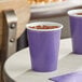 A purple Creative Converting paper cup with a drink in it on a table.