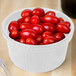 A Tablecraft white cast aluminum bowl filled with cherry tomatoes on a wooden table.