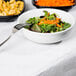 A bowl of salad with a fork on a table with a white table cover.