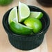 A Tablecraft hunter green cast aluminum bowl filled with limes on a counter.