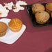 A table with a Creative Converting burgundy table cover with a plate of muffins.