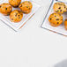 A plate of muffins on a white table with a white Tissue / Poly table cover on it.