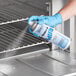 A person in blue gloves spraying Noble Chemical Nukleen oven and grill cleaner from a can.