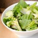 A CAC bone white porcelain salad bowl filled with lettuce and tomatoes on a table.