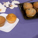 A table with a purple Creative Converting tissue/poly table cover with plates of muffins on it.