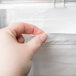 A hand pulling a napkin from a stainless steel napkin dispenser.