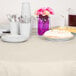 A round table set with ivory table cover, plates, and utensils.