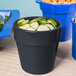 A black Tablecraft condiment bowl with cucumbers and a blue bowl of croutons on a table.