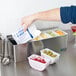 A person using a San Jamar stainless steel condiment bar to put cherries in a small white container.