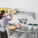 A woman in a white apron using a Regency stainless steel wall shelf in a professional kitchen.