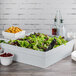 A salad in a Tablecraft gray cast aluminum square bowl on a table.