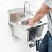 A man washing his hands in an Eagle Group stainless steel wall mount hand sink with knee pedals.