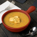 A Tablecraft copper cast aluminum soup bowl with croutons on top next to a spoon and fork.