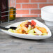 A white Tablecraft cast aluminum triangle display bowl filled with fruit on a table.