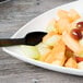 A Tablecraft white cast aluminum triangle display bowl filled with fruit on a table.