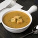 A white Tablecraft cast aluminum soup bowl with croutons and a spoon next to it.