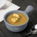 A Tablecraft gray cast aluminum soup bowl with a spoon next to it.