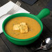 A green Tablecraft cast aluminum soup bowl with a spoon next to it.