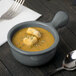 A Tablecraft granite cast aluminum soup bowl with a spoon next to it.