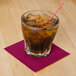 A glass with ice and a straw with a red cocktail napkin on a counter.