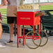 A man standing next to a red Carnival King popcorn cart filled with popcorn.