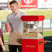 A man standing next to a Carnival King commercial popcorn machine with a bag of popcorn.