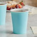 Two Creative Converting pastel blue paper cups on a table with a pastry.