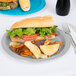 A sandwich with lettuce and tomato and potato chips on a Creative Converting Shimmering Silver paper plate with a fork.