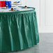 A table with a hunter green Creative Converting plastic table skirt on it.