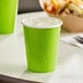 A Fresh Lime Green Creative Converting paper cup with ice in it on a table.
