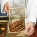 A gloved hand using a Cambro amber plastic colander pan to hold sausages.