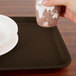 A hand holding a paper cup over a Brazil brown rectangular tray.