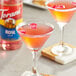 A glass of pink liquid with rose petals in it, with a Torani Rose Flavoring Syrup bottle on the table.